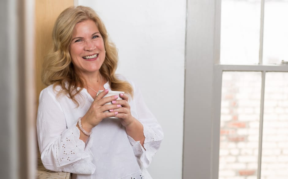 Deanna Moffitt smiling with a cup of coffee in a brightly lit room