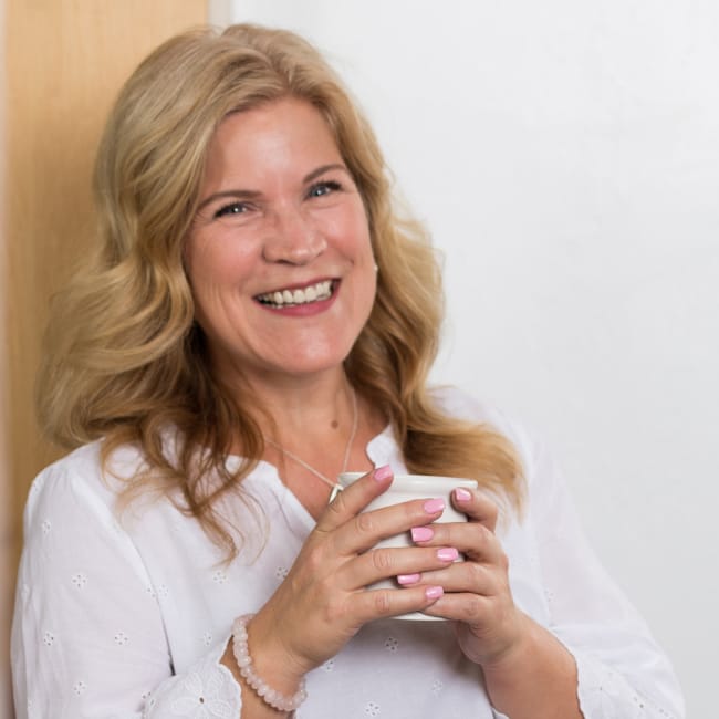 Deanna Moffitt smiling with a cup of coffee in a brightly lit room